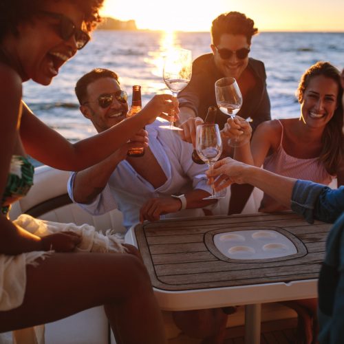 Group of smiling young people toasting at boat party during sunset. Men and women enjoying at a boat party.